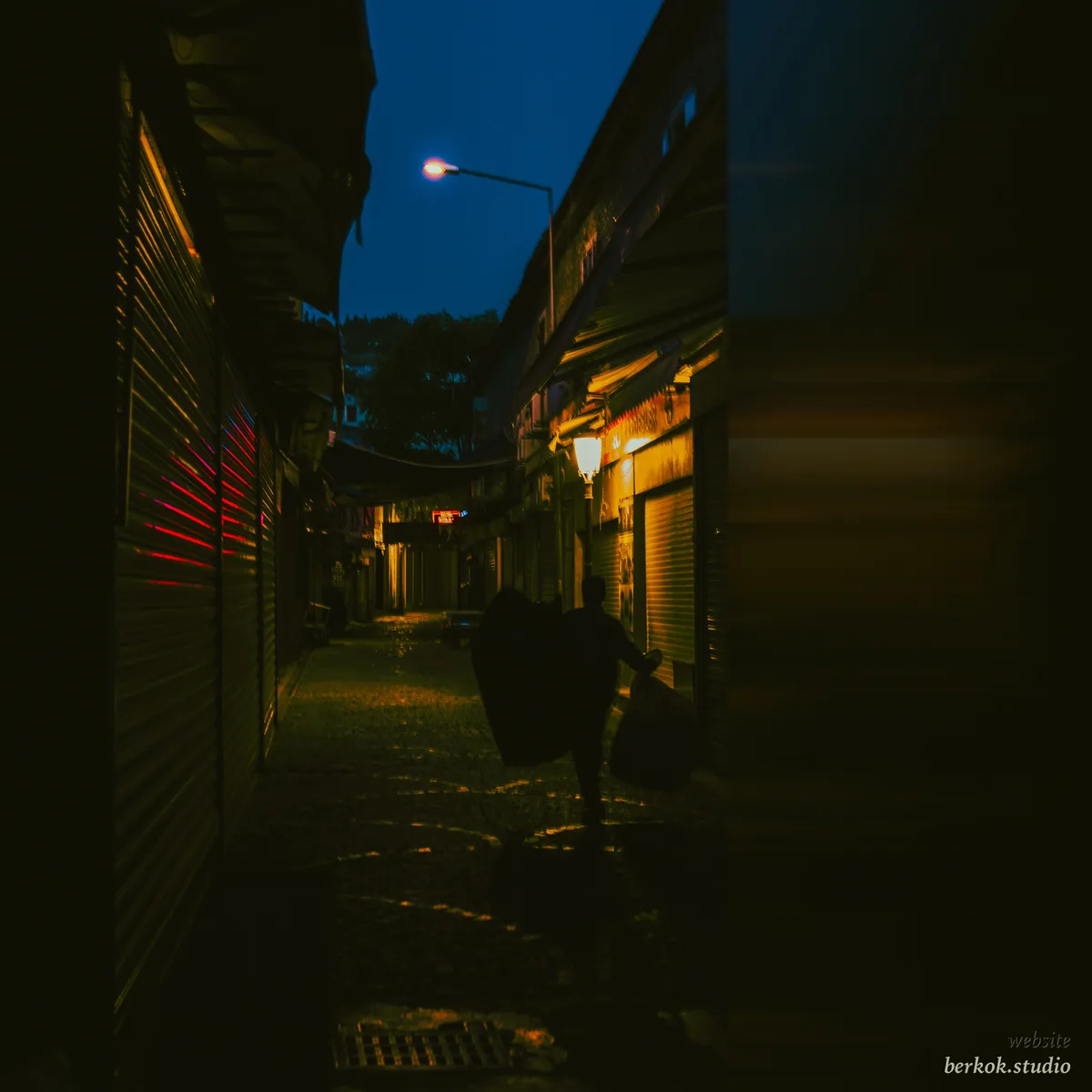 A person walking through a dim market alley at blue hour