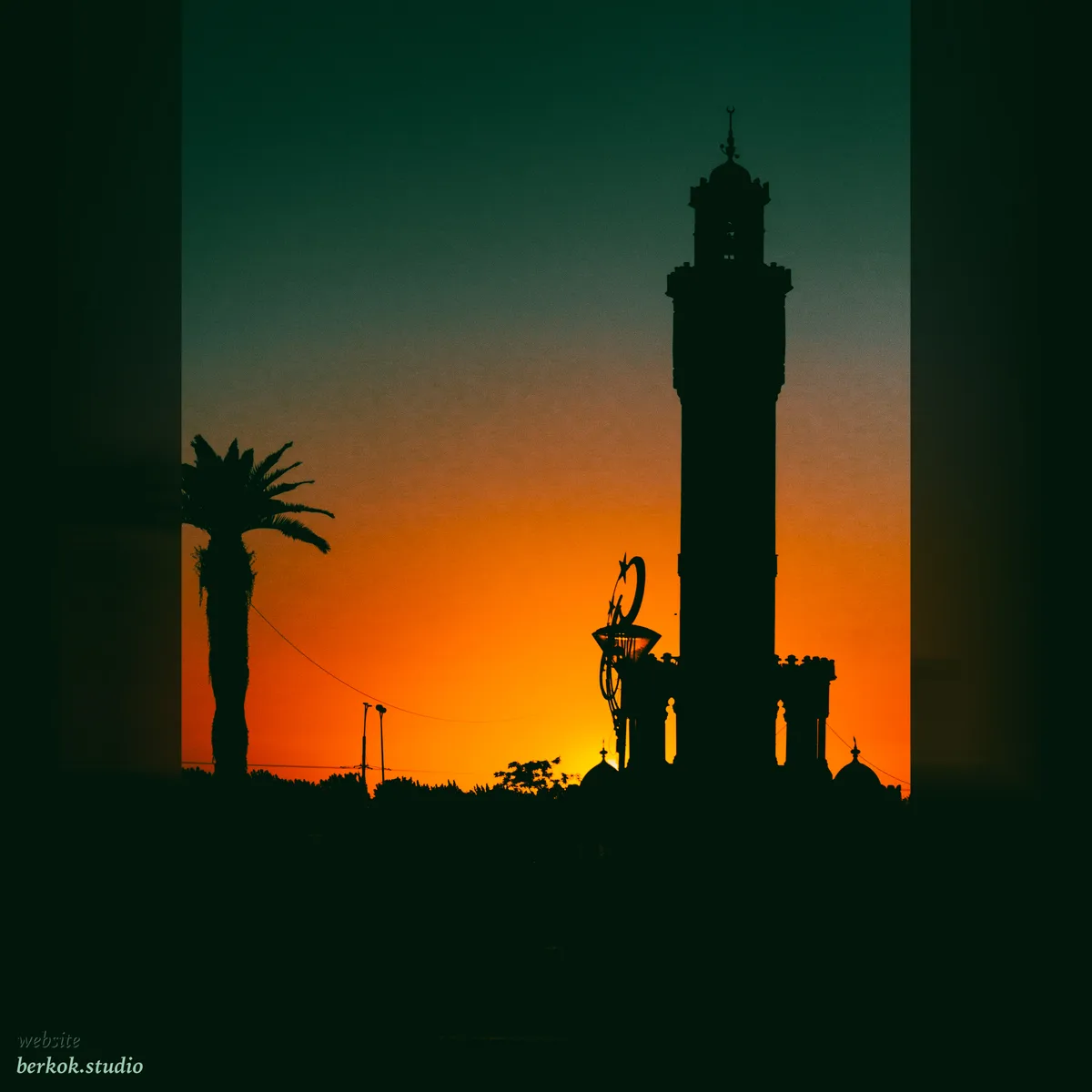 A minaret and palm tree silhouetted against an orange sunset
